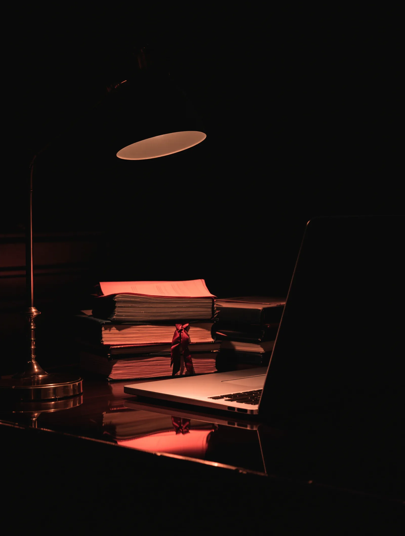 A lawyer's desk at night: laptop, bound files and a brass lamp